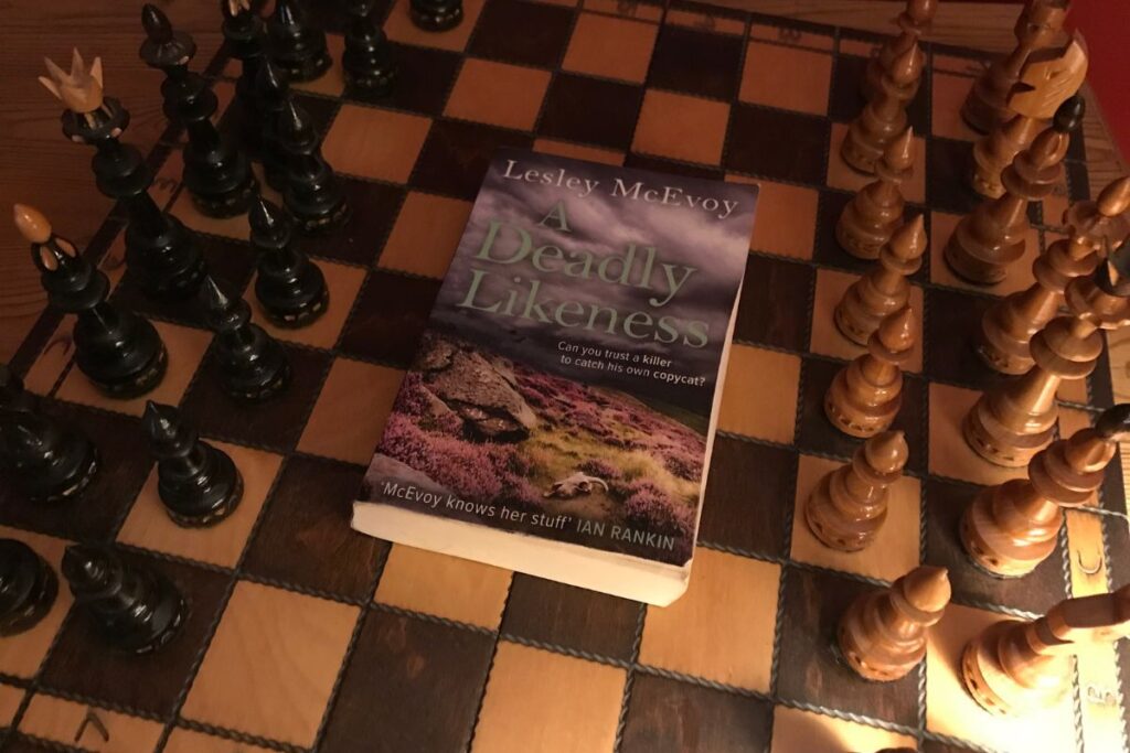 A Deadly Likeness by Lesley McEvoy on a dimly lit chess board