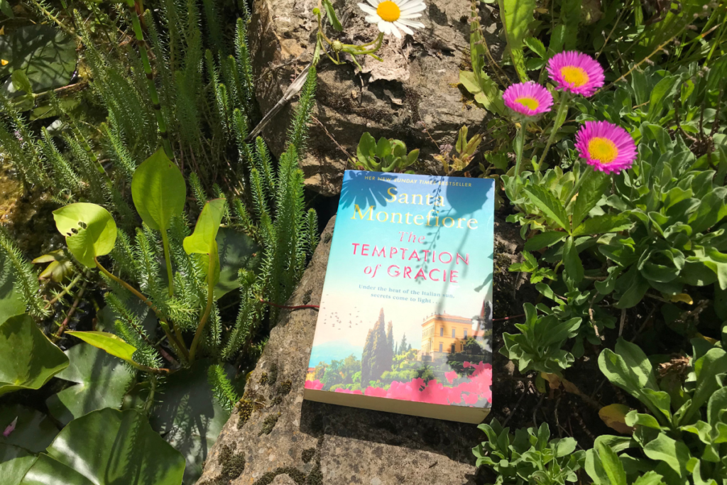 The Temptation of Gracie by Santa Montefiore resting on a stone in a sunny garden