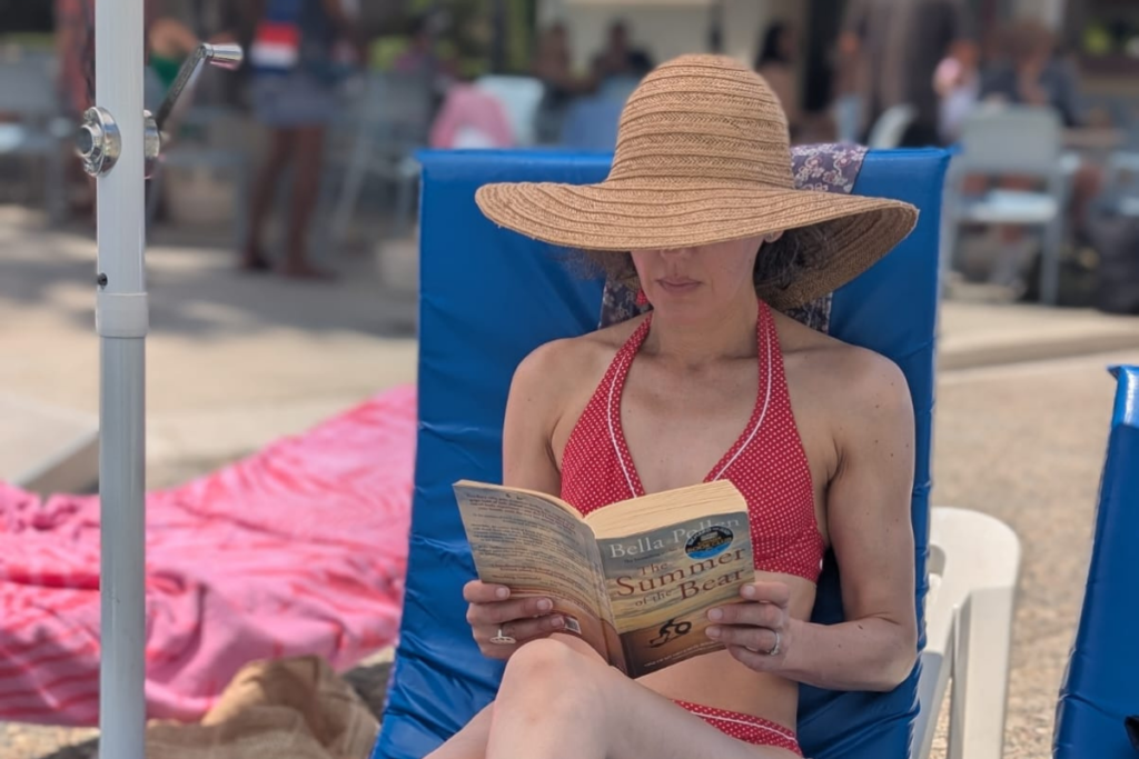 A woman reading The Summer of the Bear by Bella Pollen on a sun lounger by the pool